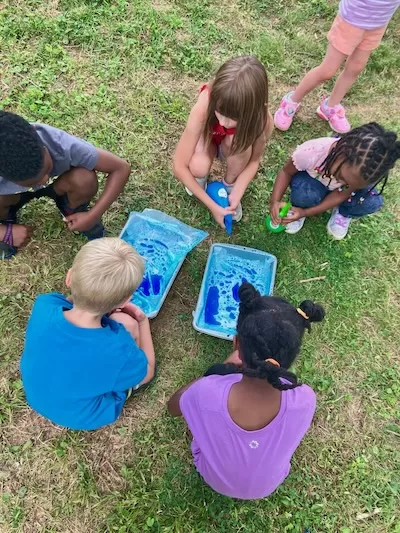 4 children gaethered around trays outside doing an experiment